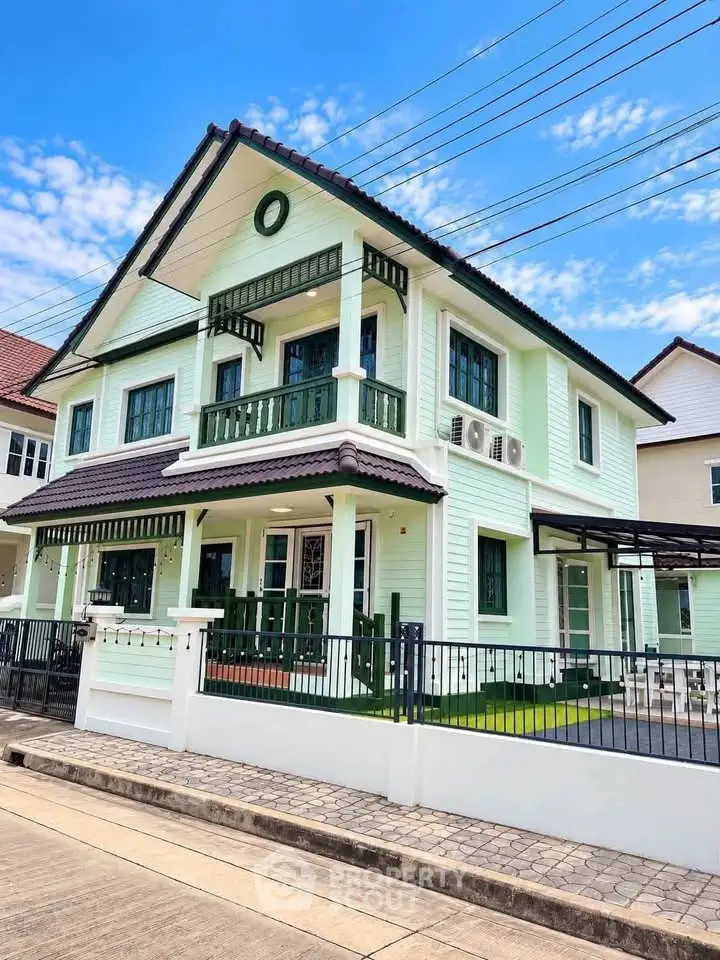 Charming two-story house with green facade and balcony, featuring a modern design and spacious outdoor area.
