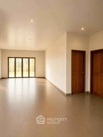 Spacious empty room with large windows and wooden doors, perfect for customization.