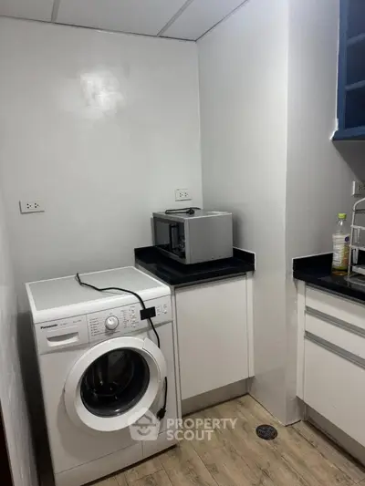 Compact kitchen with washing machine and microwave, efficient use of space.