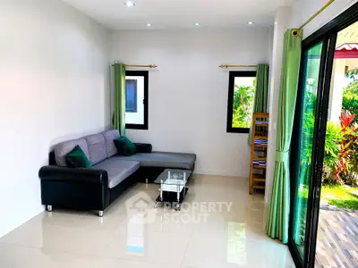 Bright living room with modern sofa and glass coffee table, opening to lush garden view.