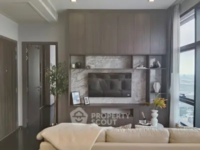 Modern living room with sleek TV setup and large windows offering city views.