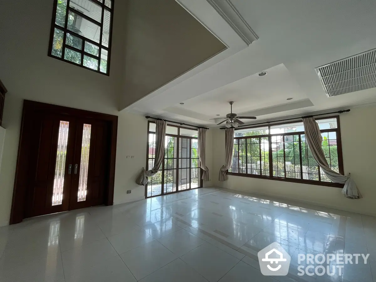 Spacious living room with high ceilings, glossy tiled flooring, and ample natural light from large windows and French doors leading to a balcony.