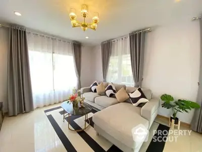 Elegant living room with plush white sofa, chic black and white rug, and modern gold chandeliers, bathed in natural light from large windows.