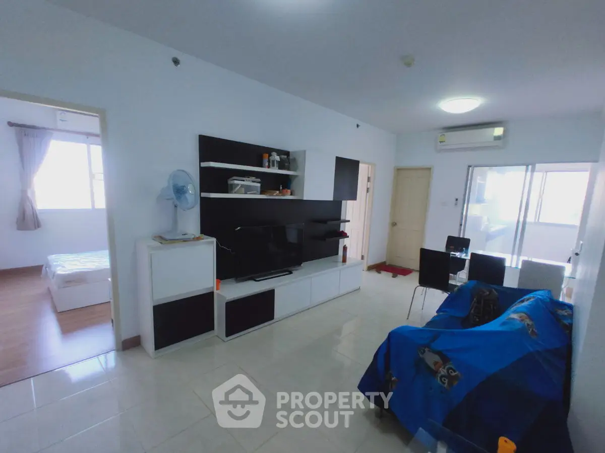 Spacious living room with modern entertainment center and dining area, adjacent to a bright bedroom.