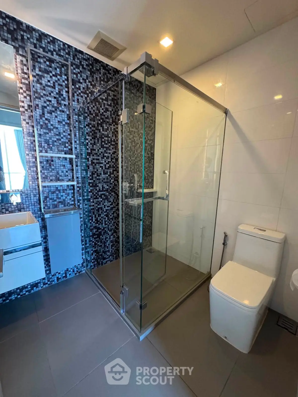 Modern bathroom with glass shower enclosure and mosaic tile accent wall.
