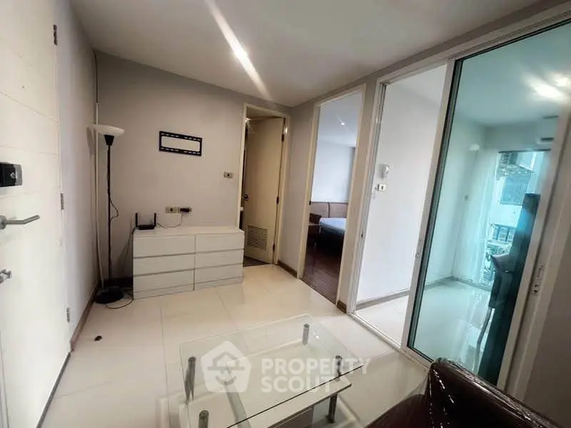 Modern apartment interior with sleek design and glass elements, featuring a cozy living area and bedroom access.