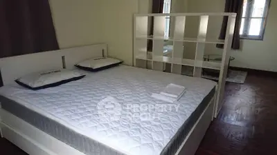 Spacious bedroom with modern white bed and partition, hardwood floors, and natural light.