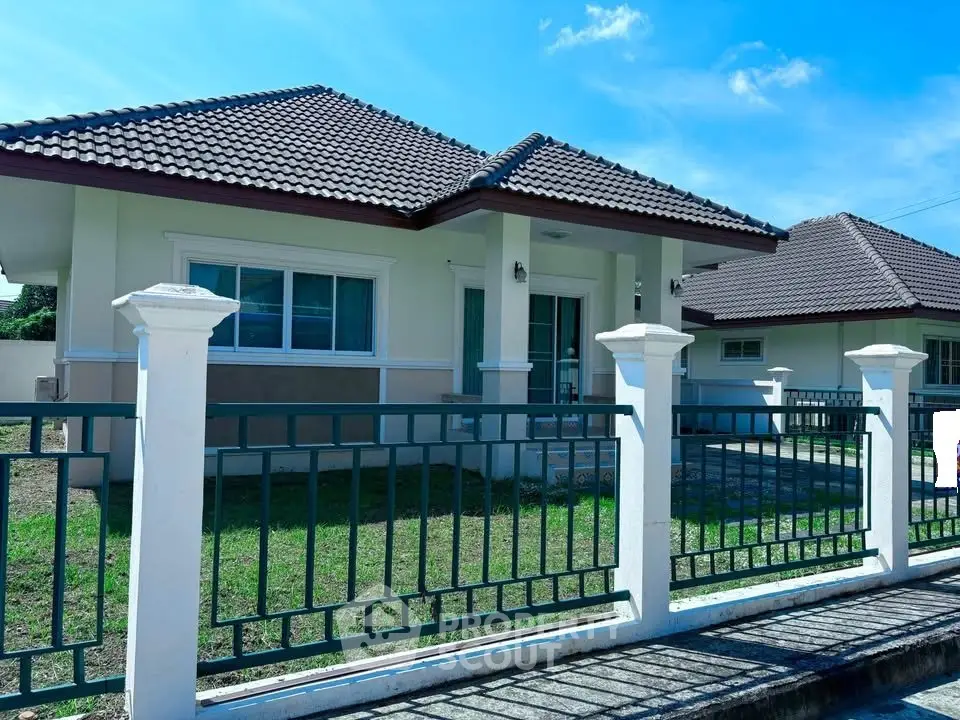 Charming single-story house with tiled roof and fenced yard under clear blue sky.