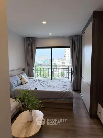 Modern bedroom with large window and city view, featuring cozy decor and wooden flooring.