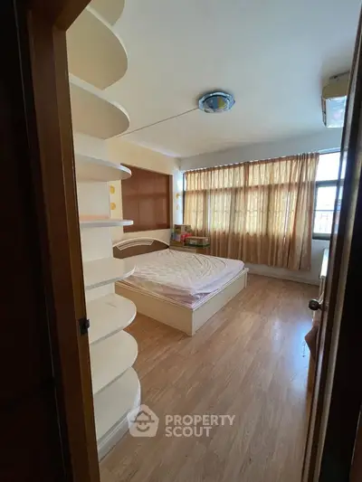 Cozy bedroom with wooden flooring and large window for natural light