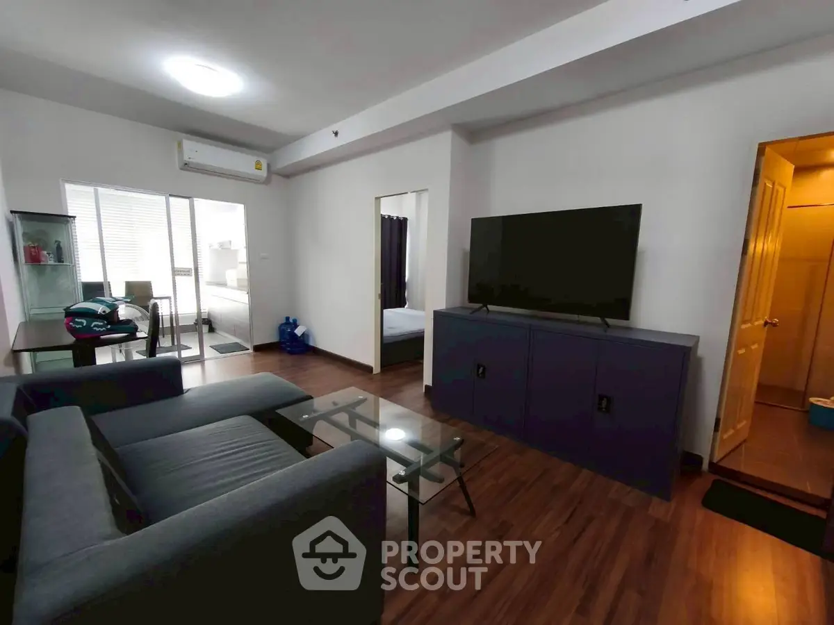 Modern living room with sleek furniture and large TV, open layout to dining area.