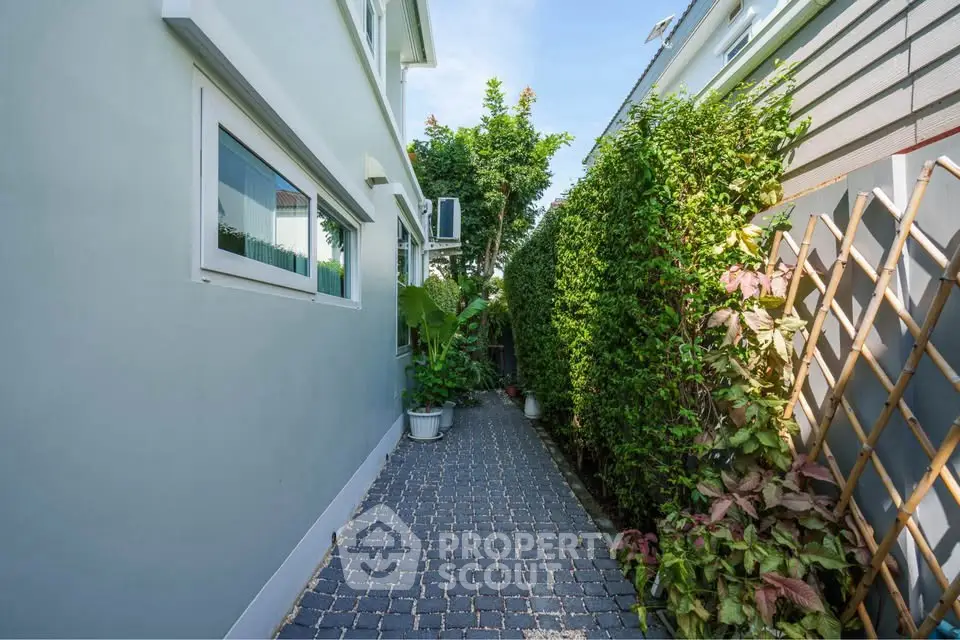 Charming garden pathway beside modern home with lush greenery and potted plants.