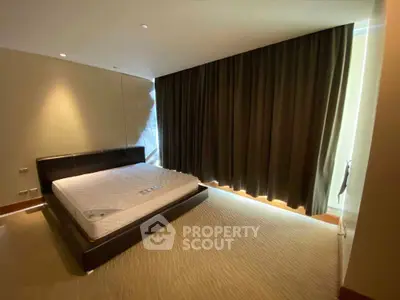 Spacious bedroom with large bed and floor-to-ceiling curtains in modern apartment.