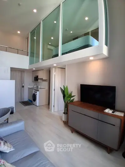 Modern loft apartment with mezzanine, stylish living area, and compact kitchen featuring washing machine.