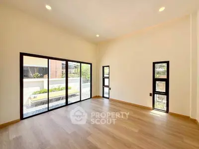 Spacious modern living room with large windows and wooden flooring, offering abundant natural light.