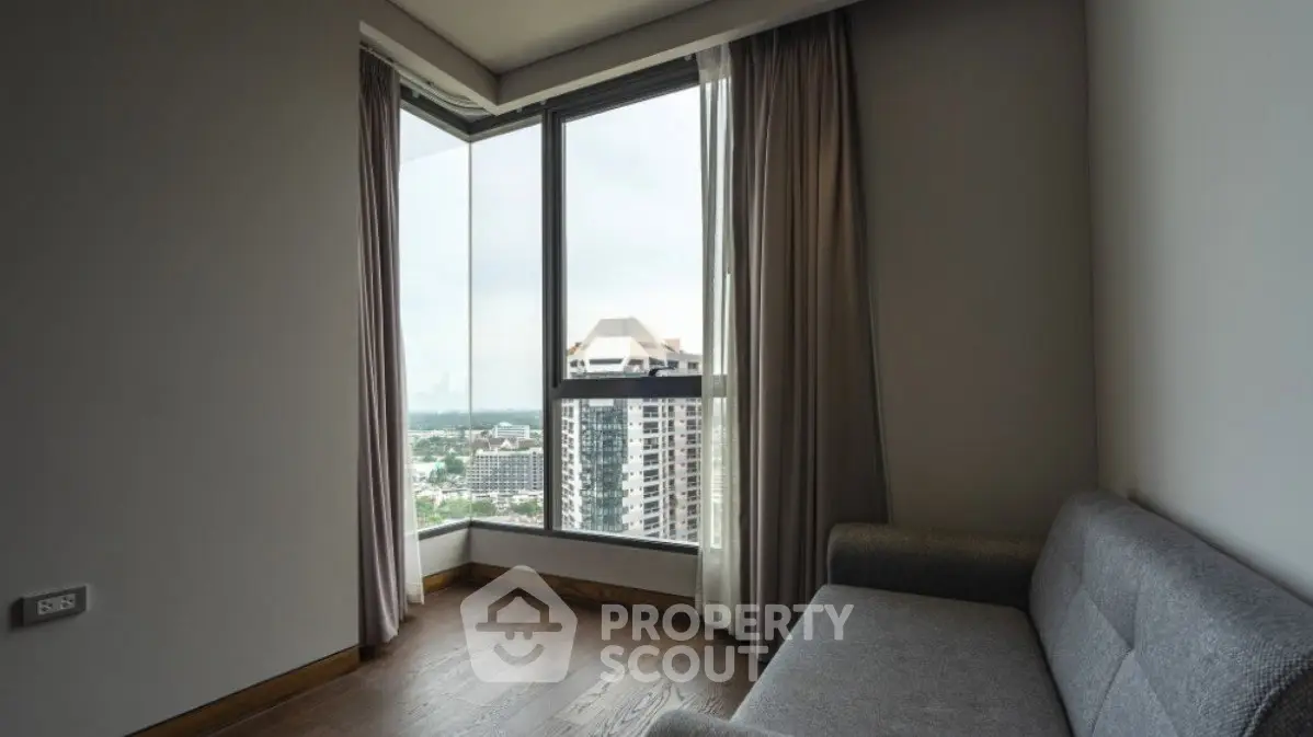 Modern apartment corner with large windows and city view, featuring a cozy gray sofa.