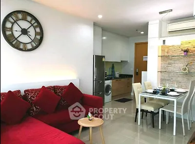 Modern living room with red sofa, wall clock, and open kitchen layout featuring dining area and appliances.