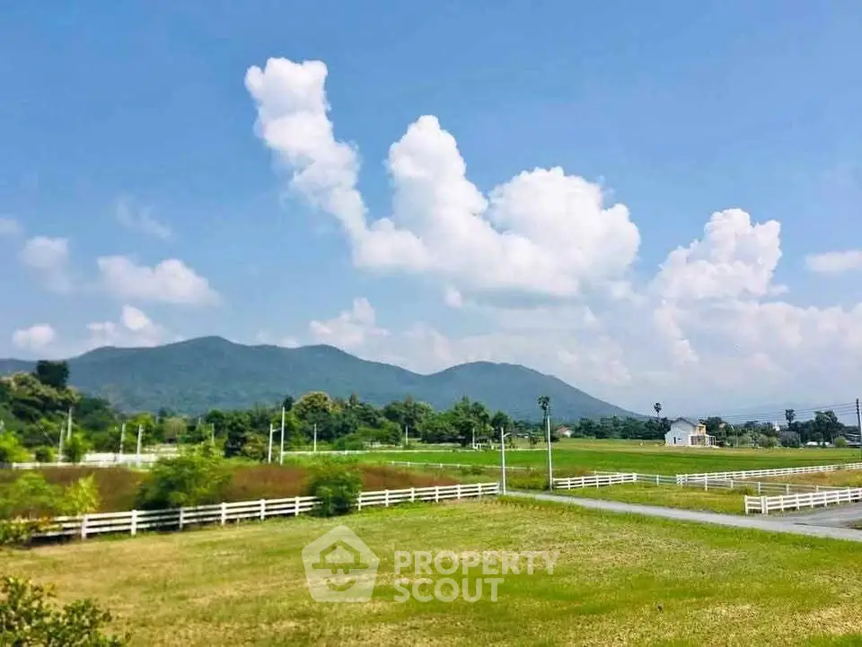 Scenic view of lush green fields with mountains and blue sky, ideal for real estate development.