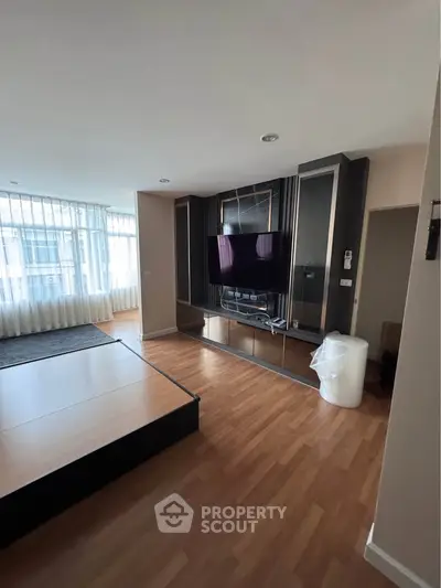 Spacious living room with modern TV setup and large windows for natural light.