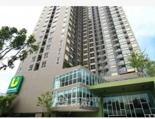 Modern high-rise condominium with sleek glass facade and lush greenery at entrance.