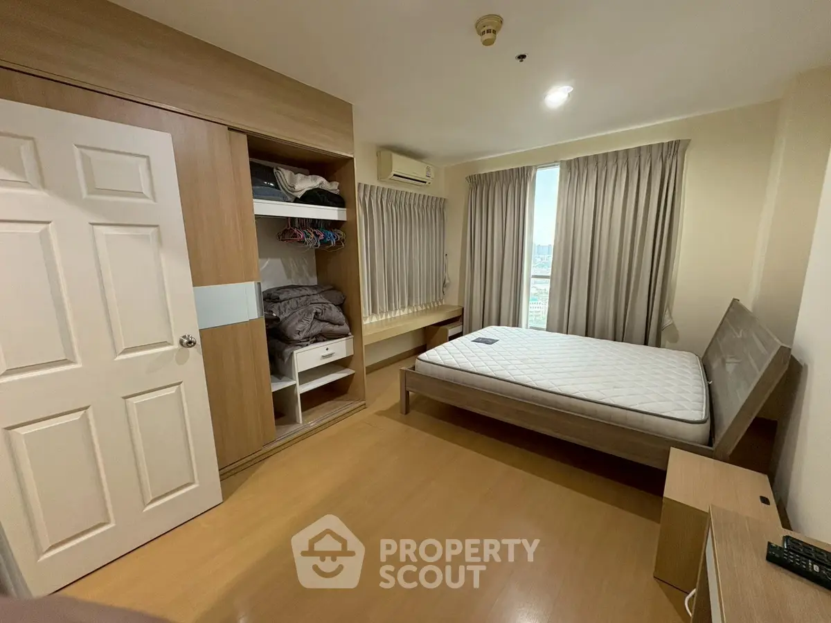 Cozy bedroom with wooden flooring, built-in wardrobe, and large window with city view.