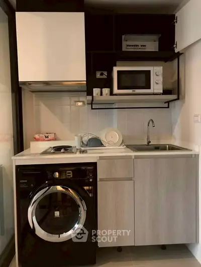Compact modern kitchen with washing machine and microwave in stylish apartment.