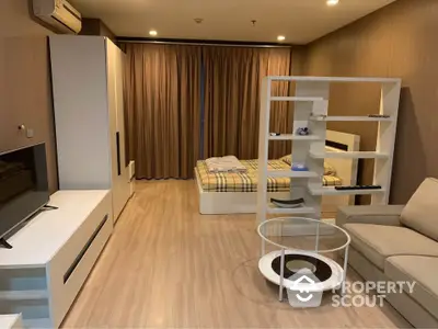 Modern studio apartment with integrated living and sleeping area, featuring sleek furniture, wooden flooring, and warm ambient lighting.