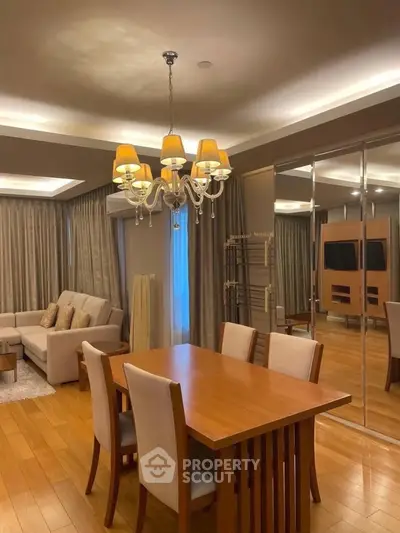 Elegant living room with dining area, wooden flooring, and modern chandelier in a cozy apartment.