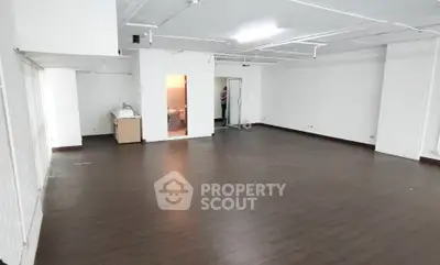 Spacious open-plan room with dark wood flooring and white walls, ideal for versatile use.