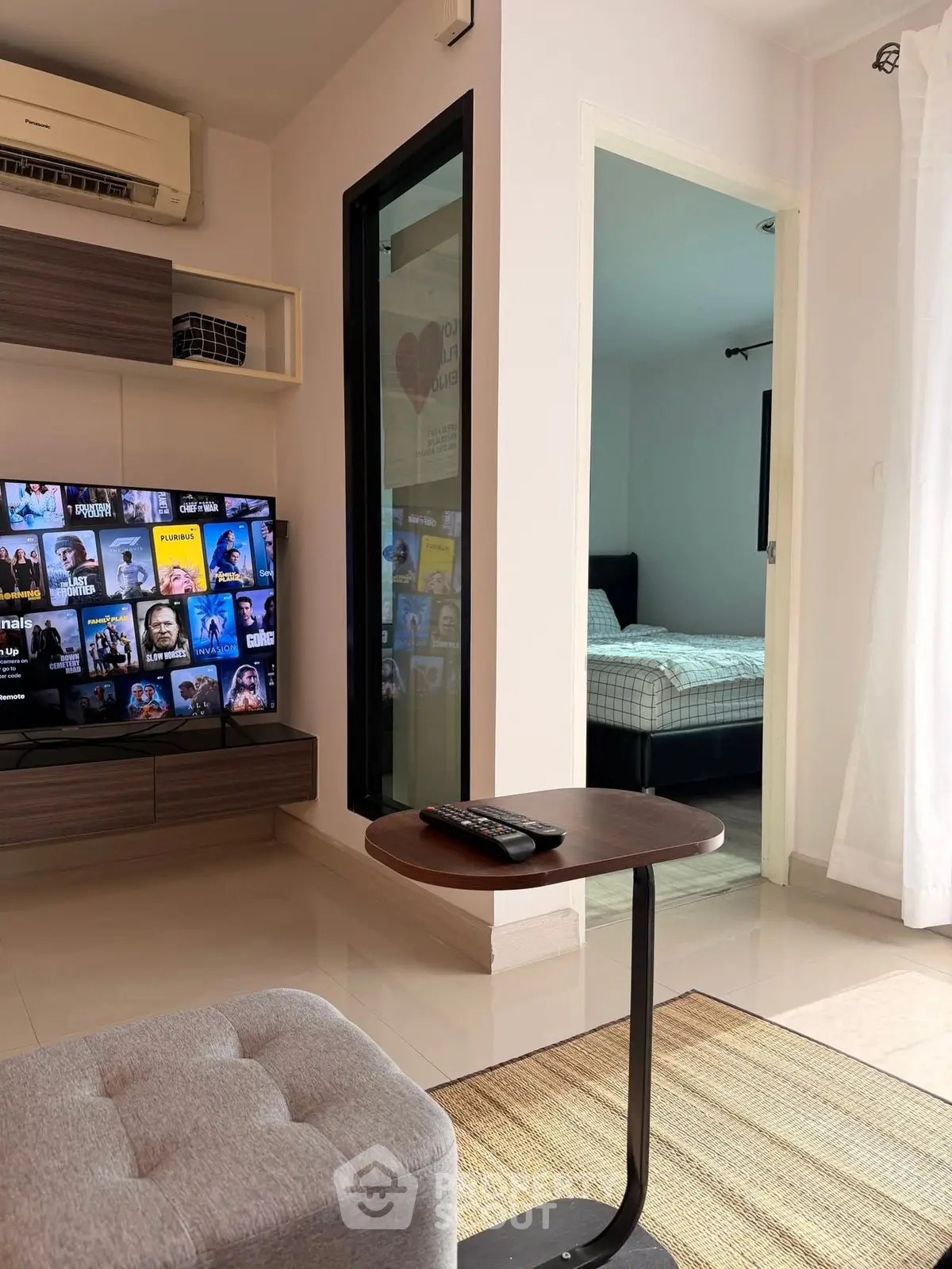 Modern living room with TV, air conditioning, and view into a cozy bedroom.