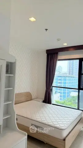 Modern bedroom with large window and city view, featuring a comfortable bed and stylish decor.