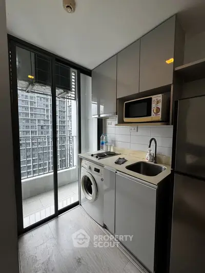 Modern compact kitchen with washing machine and microwave, featuring a balcony view in a high-rise apartment.