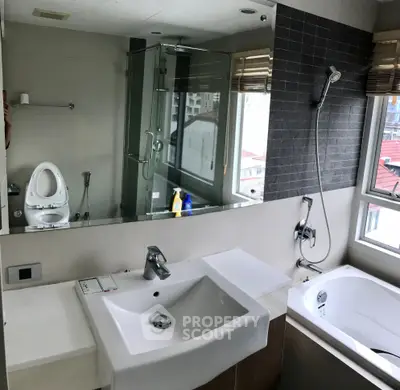 Modern bathroom with large mirror, bathtub, and city view window.