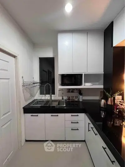 Modern kitchen with sleek black countertops and white cabinetry, featuring a built-in microwave and stylish fixtures.