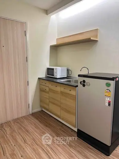 Modern compact kitchen with wooden cabinets, microwave, and mini fridge in a cozy apartment.
