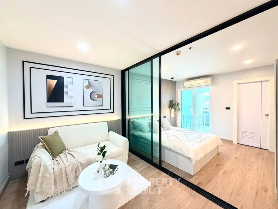 Modern open-plan living room and bedroom with stylish decor and glass partition.