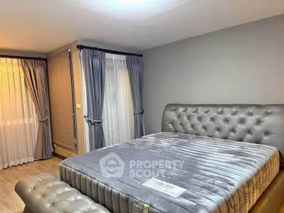 Luxurious bedroom with plush grey bed and elegant curtains in modern apartment.