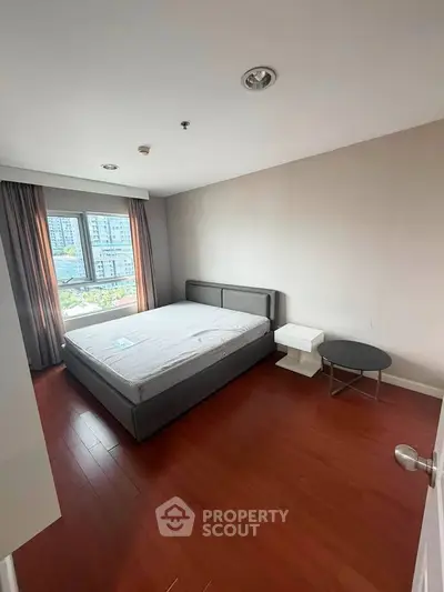 Spacious bedroom with hardwood floors and large window offering city views.