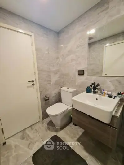 Modern bathroom with sleek fixtures and marble walls, featuring a stylish sink and toilet.