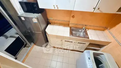 Compact kitchen with fridge, washing machine, and tiled countertops in cozy apartment.