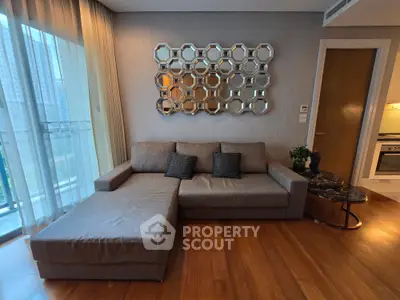 Modern living room with stylish sofa and decorative mirror, featuring wooden flooring and a glimpse of a sleek kitchen.