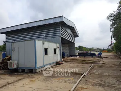 Industrial warehouse with metal siding and adjacent storage container on concrete lot.