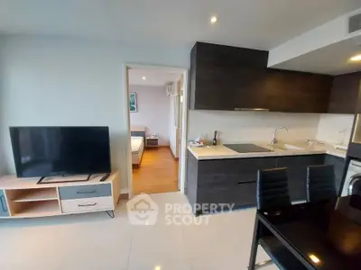 Modern open-layout kitchen and living area with sleek dark cabinets and flat-screen TV, leading to a cozy bedroom.