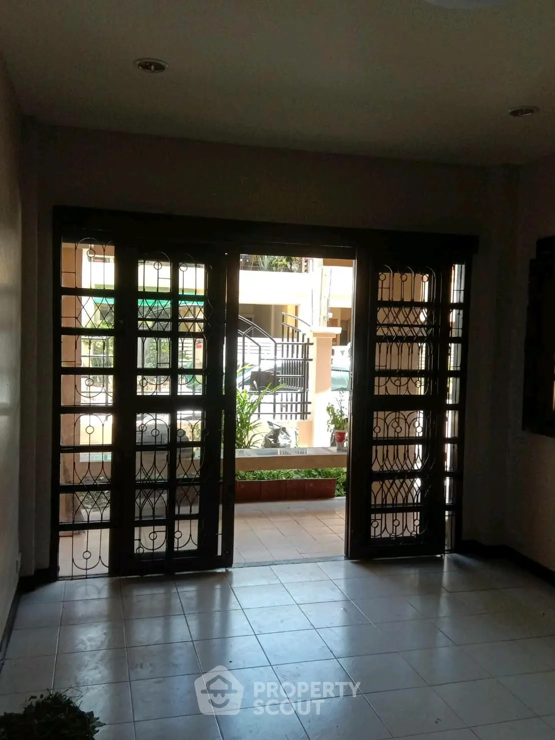 Spacious entrance with elegant ironwork doors opening to a serene garden view, perfect for welcoming guests.