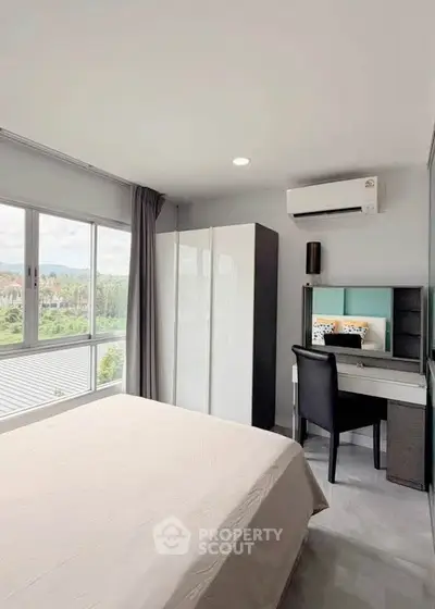 Modern bedroom with large window and study area, featuring a sleek wardrobe and air conditioning.