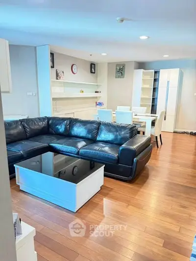 Spacious living room with modern black leather sofa and elegant dining area on wooden flooring.