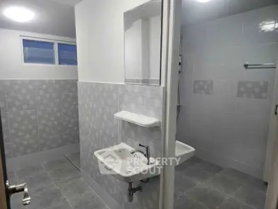 Modern bathroom with sleek design and neutral tiles, featuring a wall-mounted sink and mirror.