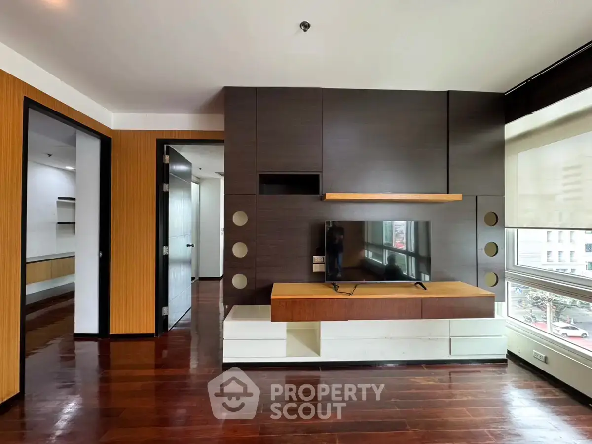 Modern living room with sleek wooden floors and built-in TV unit, offering a stylish urban view.