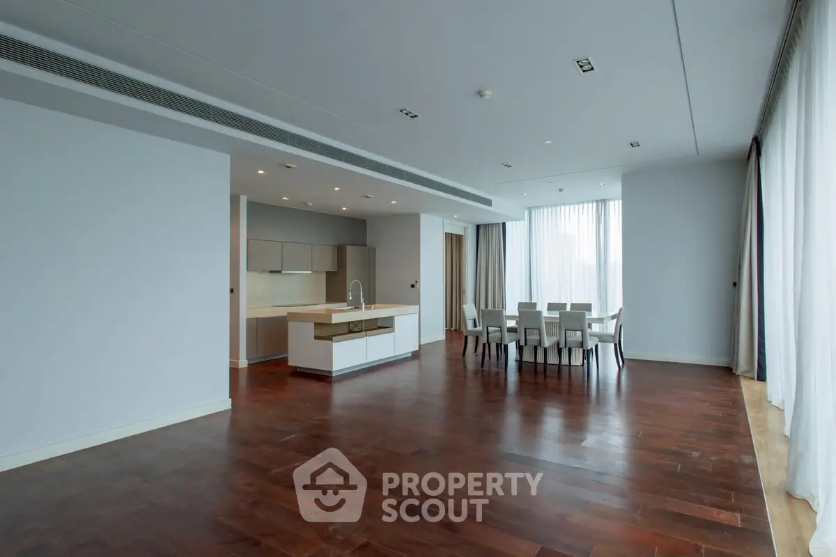 Spacious modern living room with open kitchen and dining area, featuring elegant hardwood floors and large windows.