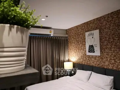 Cozy bedroom with modern decor and exposed brick wall, featuring a stylish artwork and lush greenery.